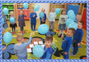 Grupa dzieci z niebiskimi balonami. Przed nimi niebieskie serce, w którym leżą obrazki przedstawiające prawa dziecka.